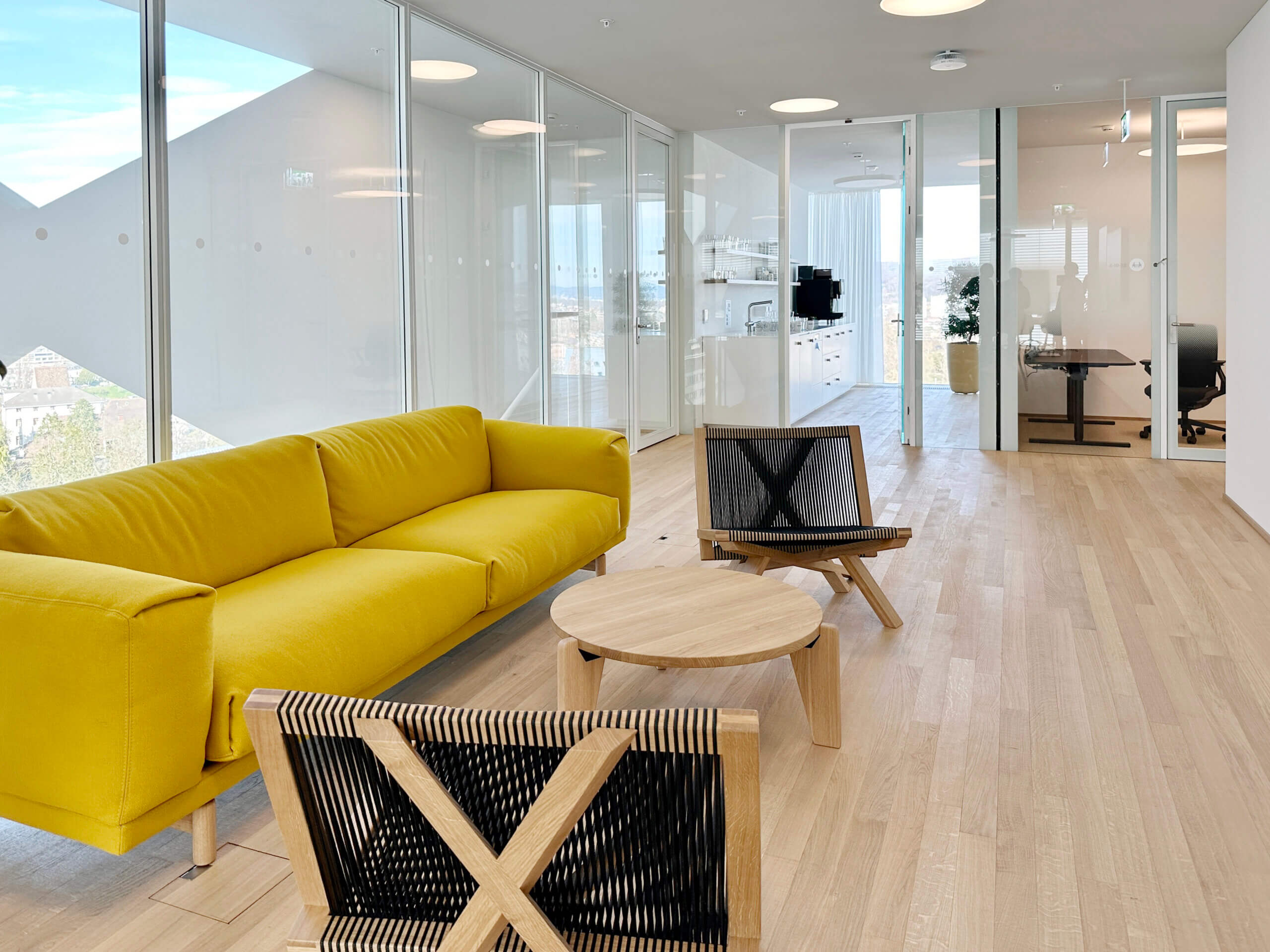 Modernes Interieur mit einem handgefertigten Holztisch und kontrastreichen Stühlen, unterstrichen durch natürliches Licht und einen ruhigen Stadtblick. Schlichte Eleganz trifft auf handwerkliches Design.